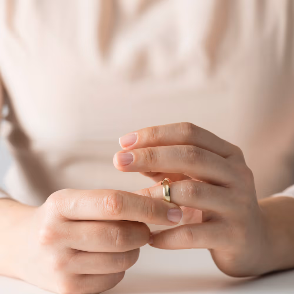 Close-up of hands removing a gold wedding ring from the ring finger.